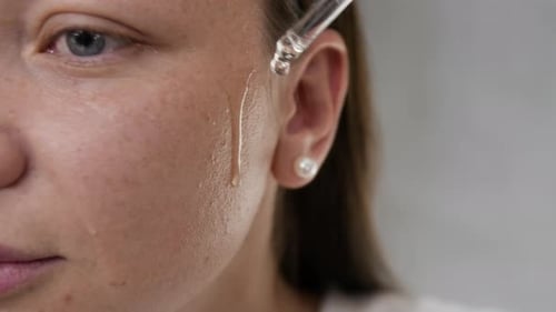 Close-up of Half Face of Young Woman Applying Serum to Cheekbones Using Dropper