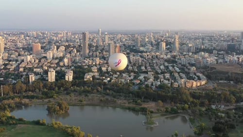 Aerial Shot Of Hot Air Balloon Descending Over Yarkon Park Against Sky In City