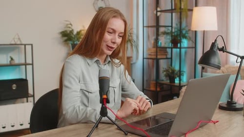 Happy Caucasian Woman Influencer Speaking Into Microphone and Laptop Webcam at Home Office Table