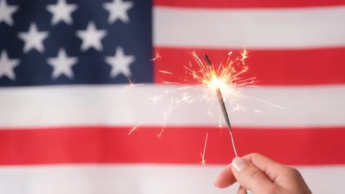 Hand Holding Sparkler in Front of American Flag