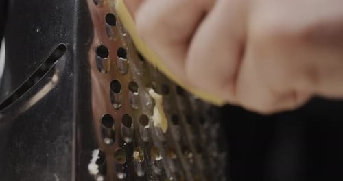A Man Rubs Hard Cheese on a Grater Closeup