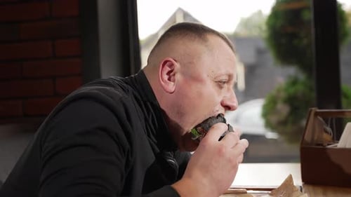 Man Enjoying Burger at Cafe Table Indoors
