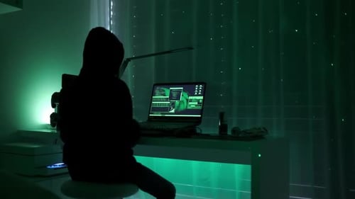a criminal hackergirl with black hood using laptop and big computers to hack network system from her
