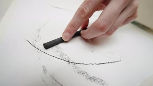 Nahaufnahme einer Hand, die mit einem Kohlestift geschwungene Linien und strukturierte Schatten Sketch