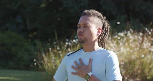 African American man closing eyes holding chest in park wearing watch taking deep breaths relaxing