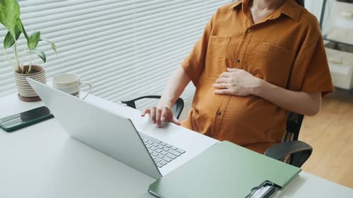 Anonymous Mother-to-be Doing Report on Laptop at Office Desk