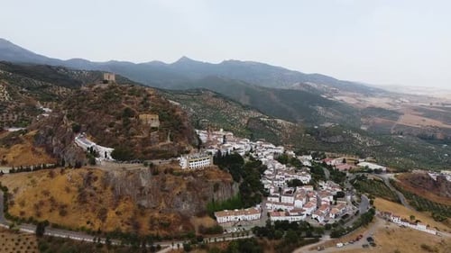 Aerial shot of medieval castle on top of a hill and traditional white houses town. Mountains in the