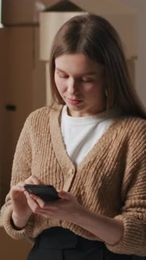 Woman Using Smartphone in Home with Moving Boxes