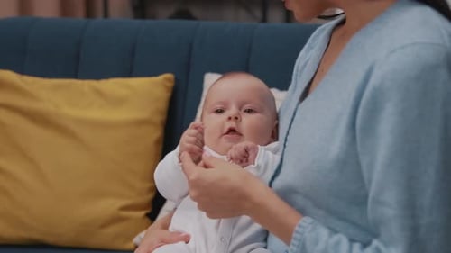 Close Up Face Cute Funny Newborn Baby Lying in Mother Arms Sitting on a Couch in a Modern Apartment