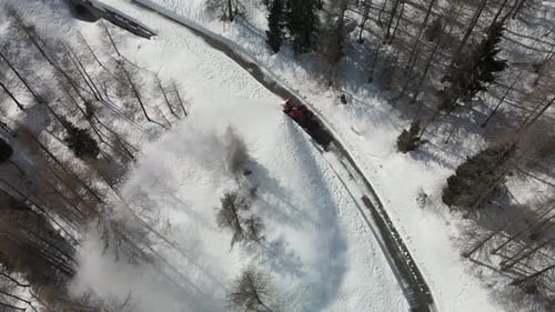 Snowplow truck removing snow from road. Aerial view of white snowy forest