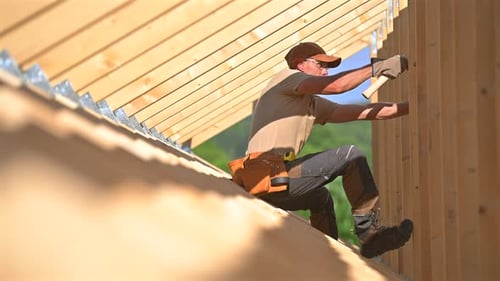 Skilled Contractor Works on Wooden Roof Structure in Bright Sunlight on Construction Site