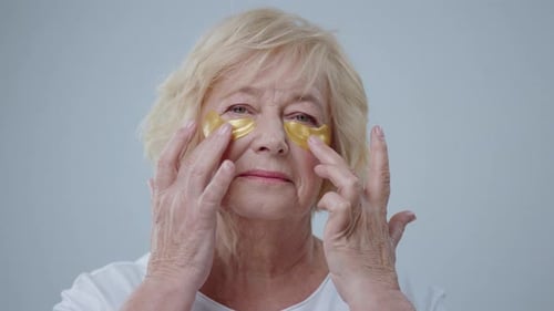 Senior Woman Applies Gold Eye Patches to Face