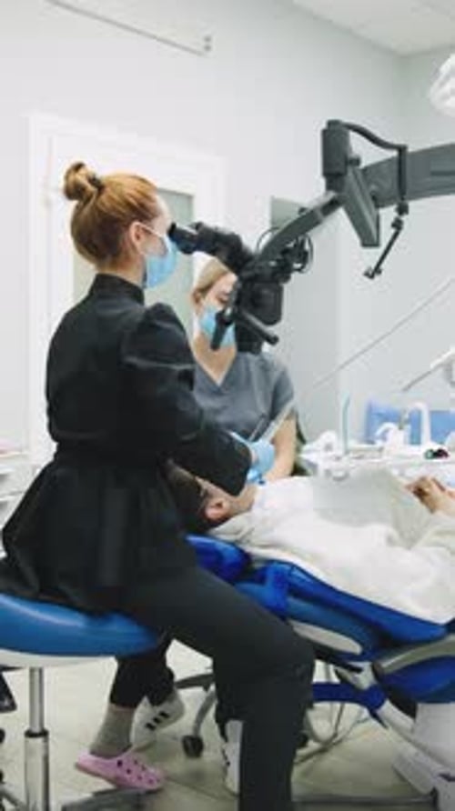 Besuch einer Zahnklinik, bei der ein Zahnarzt die Zähne eines Patienten mit einem Mikroskop untersucht, während er als Assistent tätig ist