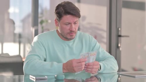 Man Counting Hundred Dollar Bills at Desk Indoors