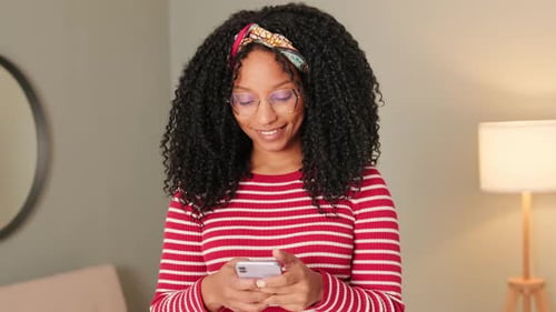 Lächelnde Frau steht im Wohnzimmer und schreibt SMS-Handy
