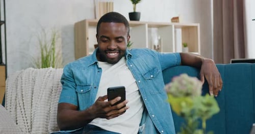 Man Smiling While Using Cellphone on Sofa