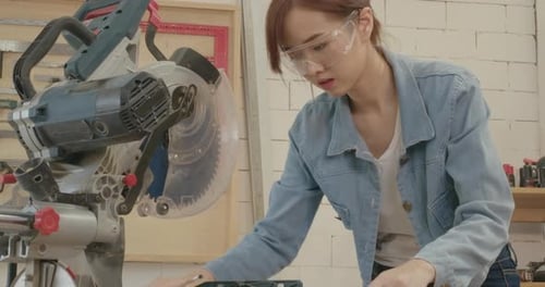 Worker young asian woman carpenter building design drawing blueprint and cutting wooden