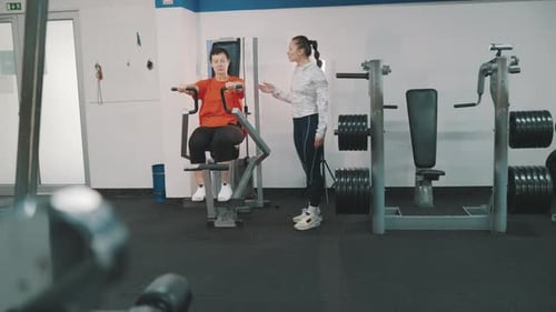 Personal Fitness Trainer Assisting Woman Exercising on Pec Deck Machine