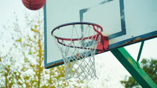Orangefarbener Basketballball, der durch den Korb fällt, mit Netz an einem sonnigen Sommertag, Nahaufnahme auf dem Hintergrund von