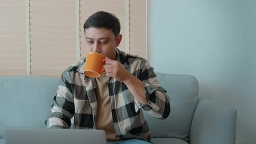 Man Working on Laptop From Home Drinking Coffee