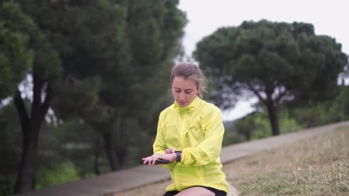 Young Woman Runner Checks Watch In Park