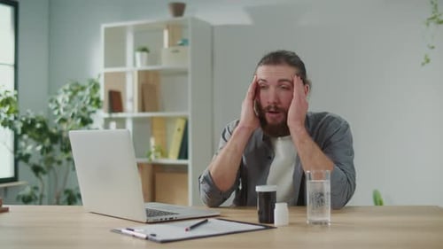 Man Rubbing Temples Experiencing Headache at Desk