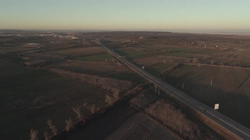 An aerial view of a highway running through agricultural fields with a few cars traveling along the