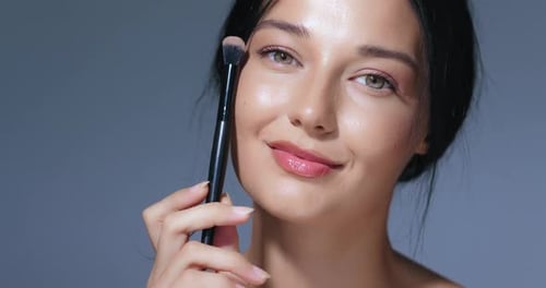 Young Woman Poses with Makeup Brush in Studio