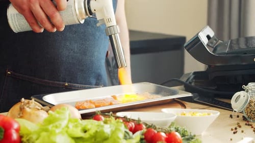 Chef Blow Torching Salmon Pieces in Kitchen