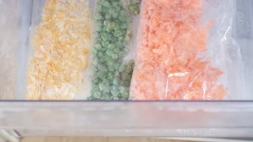 Female hand folds plastic bags with chopped vegetables into the freezer, top view close-up.