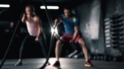 A Fitness Athletes are Training Using Battle Ropes in the Dark Gym