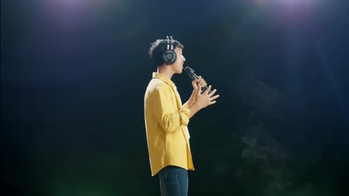 Side View Of Young Asian Boy With Headphone Singing On The White Smoke Black Background
