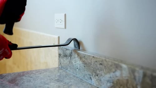 Worker Removing Old Kitchen or Bathroom Furniture During Home Renovation Using Crowbar and Hammer