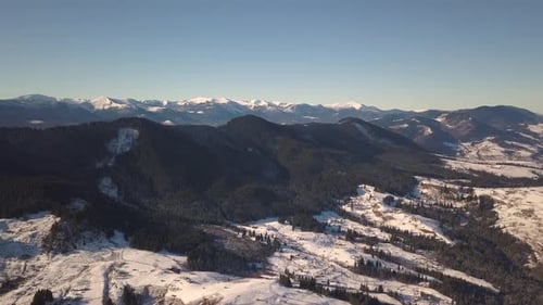 Luftbild eines kleinen Dorfes mit verstreuten Häusern auf schneebedeckten Hügeln im Winter und bei nackter Dunkelheit