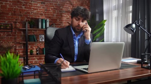 Businessman in Office Talking on Phone and Using Laptop