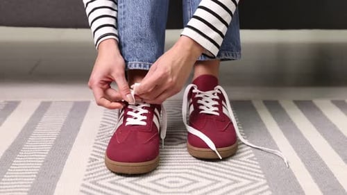 Woman tying shoelaces of red sneakers indoors, closeup