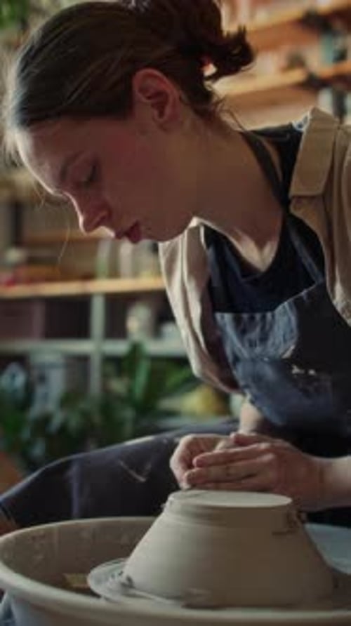 Ceramist Trimming Base of Clay Bowl with Loop Tool on Spinning Pottery Wheel