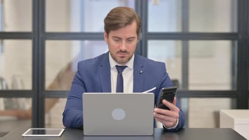 Man Using Laptop and Smartphone in Office
