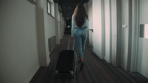 Young woman rolling luggage along hotel corridor on vacation