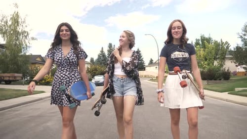 Teenage Girl Friends Walking With Skateboards On Road