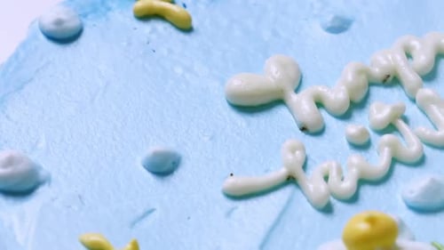 Close-up shot of the top of a birthday cake with blue frosting and decorated with white and yellow f