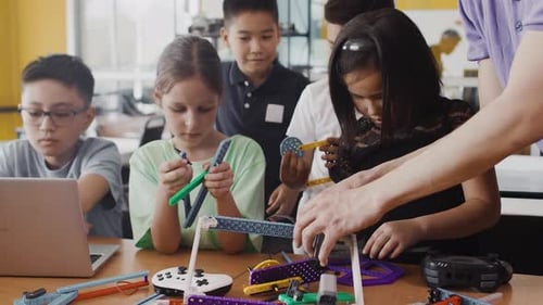 Junge Lehrerin, die Kindern in einer Klasse in einer Robotikstunde am Tisch beibringt, wie man einen zusammenbaut