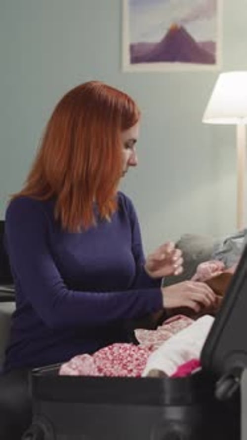 Woman Packing Suitcase with Clothing in Living Room