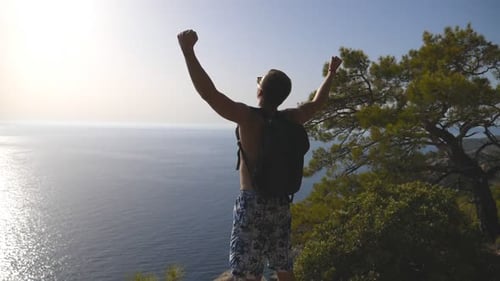 Unrecognizable Hiker with Backpack Standing on Edge of Mountain and Victoriously Raising Hands Male