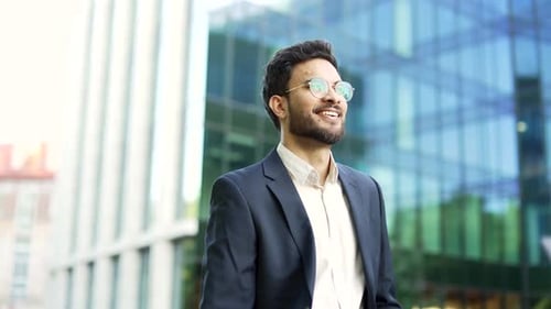 Confident businessman in a suit walks down street near an office building. Bearded entrepreneur
