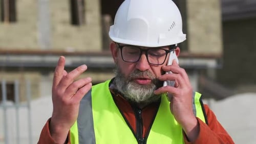 Engenheiro profissional de barba grisalha em roupas de trabalho discutindo a construção por telefone