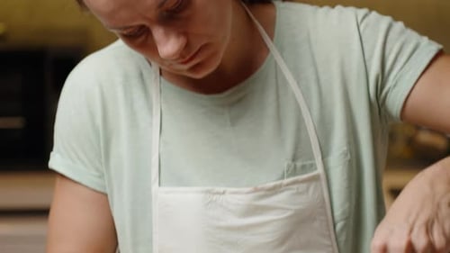 Woman Scraping Cookie Dough Into Bowl In Kitchen