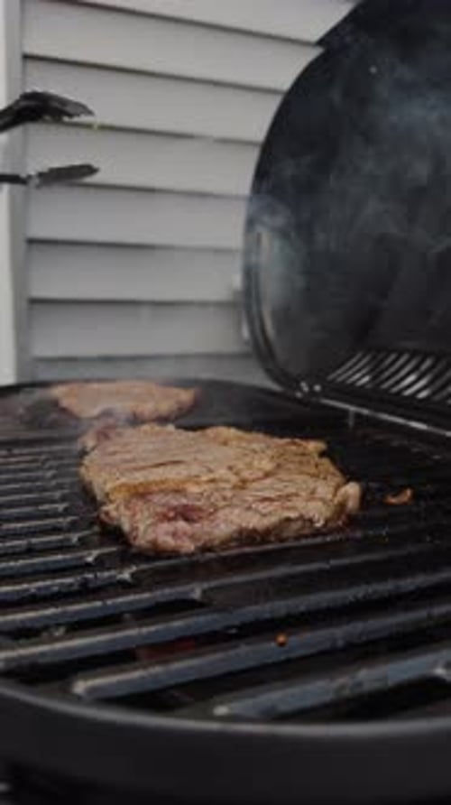 Meat Steaks Grilling and Flipping on Stove BBQ Grill Near the House Outdoor Party Food Vertical View