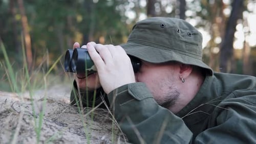 Man lying down looking through binoculars in forest