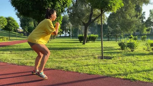 Young Woman Warms Up Exercising in Golden Sunlight of New Day in Park